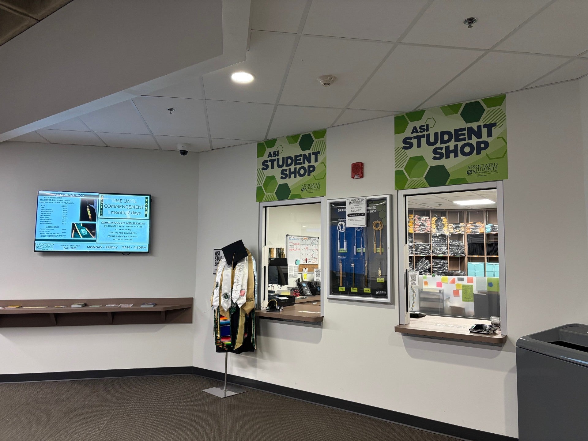 Image showing front of student shop featuring two walk up windows accompanied by displays of graduation attire including cap, gown, stoles, and tassels.